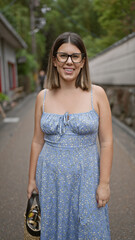 Confident hispanic woman, beautiful and joyful, cheerfully posing with glasses on, standing and smiling on kyoto's traditional streets, radiating natural and carefree latin expression.