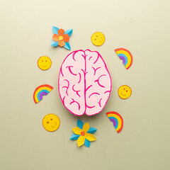 Flat layout of human brain anatomy with smile emoji, flower and rainbow made from paper on green...
