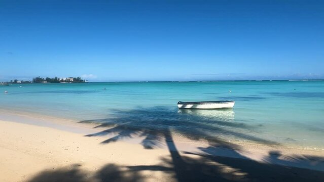 A boat in the turquoise crystal waters of a tropical island under the magnificent shade of palm trees. Pereybere Beach, Mauritius