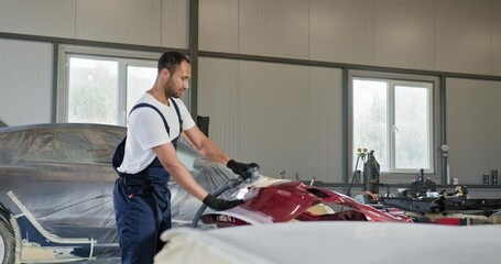 Professional auto mechanic using a polisher to repair and renew a red bumper at an automobile service station. Professional funny auto mechanic worker polishing bumper car at automobile repair