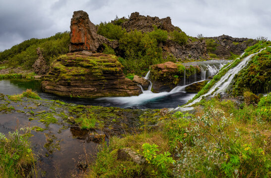 Panorama of a  beautiful fairytale-like waterfall surrounded by greenery in Gjain Valley in Iceland