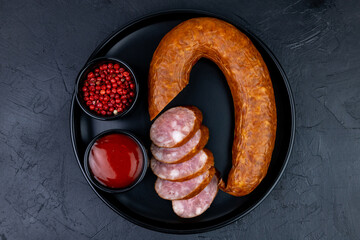 Sausage salami pieces on a black plate with spices top view