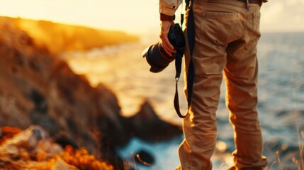 Photographer standing on a rocky coastline capturing a beautiful sunset over the ocean with a camera in hand.
