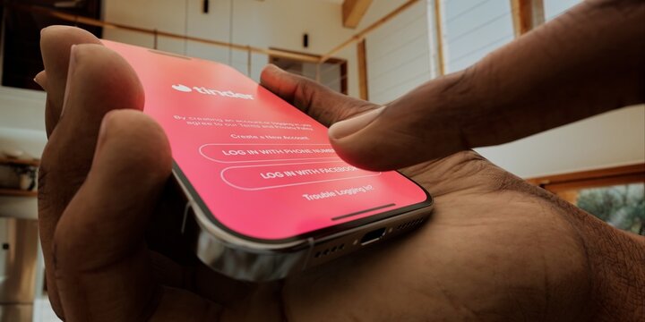Hand holding a smartphone with Tinder app open, ready to swipe in a cozy home setting