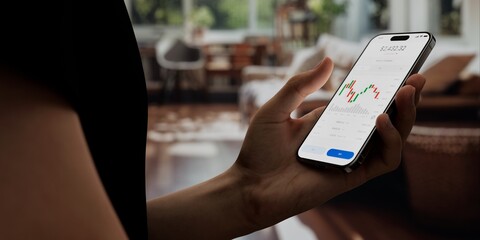 A user interacts with a stock trading app on a smartphone, displaying market charts and data, in a modern home setting. Fictional app 