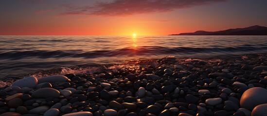Obraz premium Sunset setting on black pebble beach with small waves, perfect for copy space image.