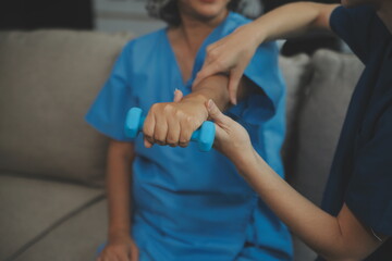 Fototapeta premium Old woman training with physiotherapist using dumbbells at home. Therapist assisting senior woman with exercises in nursing home. Elderly patient using dumbbells with outstretched arms.