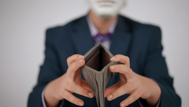 Close-up. An unrecognizable human in a white face mask and a blue suit holds an open empty leather wallet in his hands, showing it to the camera. A human waves his head negatively while sitting