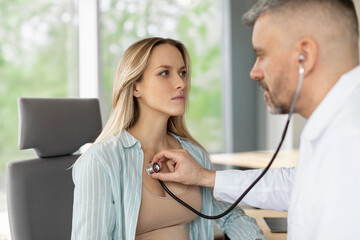 Young woman breathing while male doctor holding stethoscope on female chest, efficient general...
