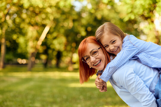 Photo of a lovely mother and her daughter on her back, laughing and enjoying the afternoon at the park.