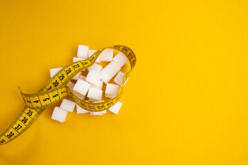 Sugar-free diet for weight loss. A pile of white sugar cubes and a yellow measuring tape on a...
