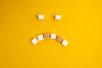 Brown and white sugar on a yellow background. A face with a smile made of sugar is sad and...