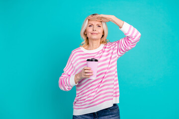 Photo of cheerful senior woman wear striped sweatshirt holding cappuccino look far arm on forehead...