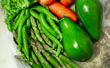 Ripe whole green avocados close up. Carrots, asparagus officinalis, green peas, green lettuce leaves.