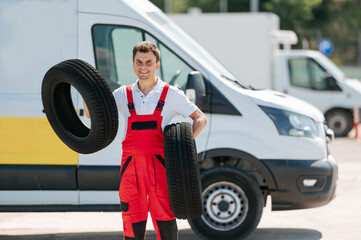 Young smiling man, in red coverall,  car mechanic holding auto tires