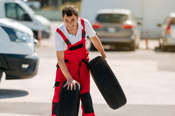 Young smiling man, in red coverall,  car mechanic holding auto tires