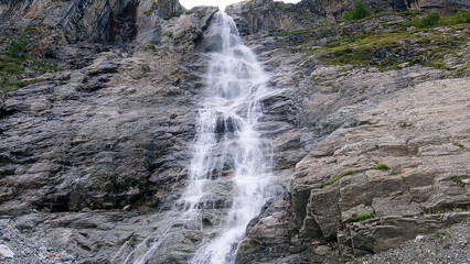 A cascading waterfall flowing down a rugged rocky mountain cliff. View from below of the most beautiful waterfall in the wilderness.