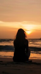 A young woman sits on the beach, watching the sunset. She is alone and contemplative, enjoying the peace and beauty of the moment.