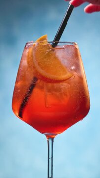 Glass of apperol spritz cocktail with orange slice and straw on blue background. the cocktail straw is placed in the glass, closeup of summer drink