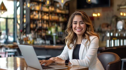 Fototapeta premium Happy young Latina businesswoman in suit working with laptop in a cafe or bar smiling confidently, for business owner, self employment, work from home, manager, small business, remote working concept.