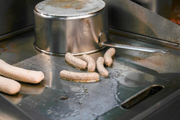 Sausages are fried on a stove in a restaurant kitchen before serving.