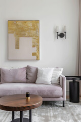 A modern living room with a light purple sofa, wall art, and a black side table. The walls have neutral tones and an accent of gold on the painting hanging above it. There's also a coffee table.