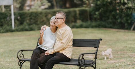 Fototapeta premium Happy old couple sitting on chairs in the park arms around shoulders