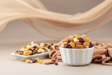 The mix of various nuts and raisins in a white bowl on a beige background.