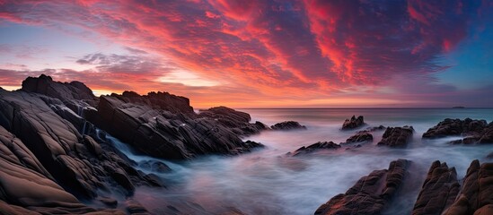 Fototapeta premium The serene scene of waves cascading over rocks in the sea under a colorful dusk sky resembles a dream, providing a captivating copy space image.
