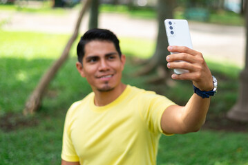 Young latin guy taking frontal selfie with smartphone outdoors. 