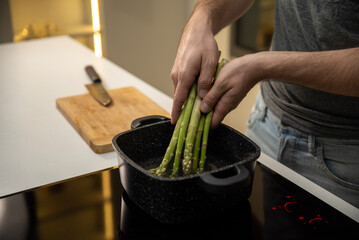 A man puts asparagus into a pan on an induction cooker