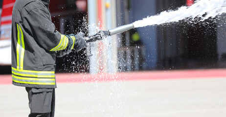 fireman with uniform spraying a lot of foam with the powerful hose nozzle to put out the fire