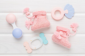 Pink baby booties and rattles on wooden background, top view