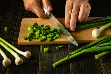 A cook cuts green garlic on a cutting board with a knife to prepare a vegetarian dish. Peasant food