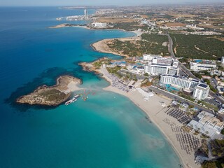 Fototapeta premium Panoramic view of Nissi Bay and the landscape. Sandy beach with Nissi island and hotel resorts in Ayia Napa. Aerial view of the Famagusta coastline towards Ayia Napa Marina. Calm sunny morning.