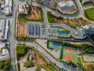 Aerial view of solar panels fitted above parking lot providing shade and electricity. Tennis courts part of hotel in Ayia Napa, Cyprus. Top down view on the colorful urban landscape in the morning.