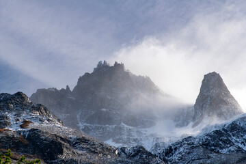 Low angle view with backlight of snow covered peaks of Cordillera Paine mountain group in Paine Massif, Torres del Paine National Park, Patagonia, Chile surrounded by white clouds