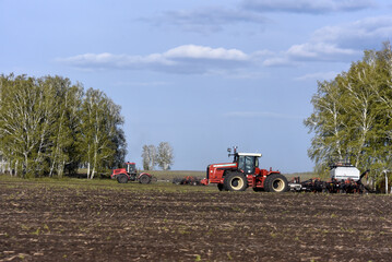 Obraz premium Agricultural machines for sowing grain in the field. Red tractors in the sowing campaign.