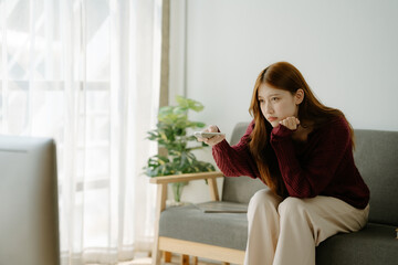Young Asian woman feeling happy, smiling and watching TV while relaxing in the living room at home.