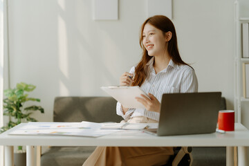 Smiling beautiful Asian girl with black hair working in cafe,Casual woman manager sitting in her office workspace with computer and big bright window and