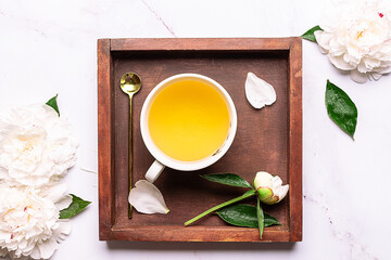 Creative composition with cup of aromatic tea on the wooden tray, decorated with aromatic peony...