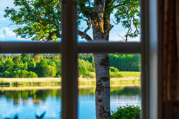 Beautiful view through a window of a serene lake with lush green trees and bushes creating a...