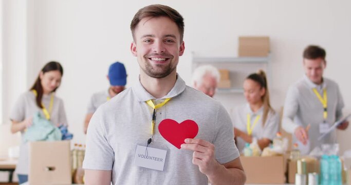 Portrait of a smiling volunteer work in humanitarian support center or service, holding a paper red heart. Commitment to donation, charity, and helping others shines through compassionate expression.