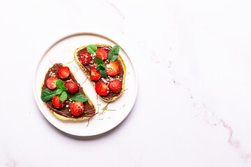 Sweet homemade toasts with chocolate paste, nuts, srtawberry and aromatic mint leaves on the...