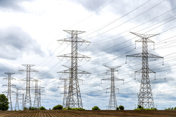 High voltage electric power distribution towers in a farm field against a cloudy sky