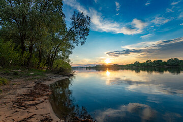 The sun gently lowering on the horizon, casting a warm glow over the tranquil water and surrounding...