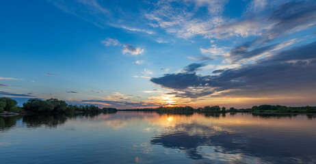 The sun sets over the water, casting a warm glow on the rippling waves, as fluffy clouds fill the...