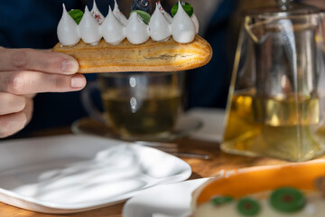 featuring a person holding a delicious eclair with whipped cream and blueberries. The eclair is...