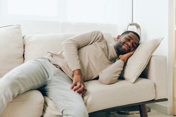 Relaxed African American Man Sitting on Sofa at Home, Enjoying a Weekend A smiling, young and...