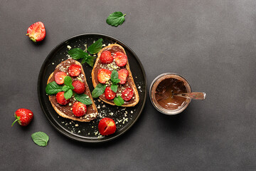 Sweet homemade toasts with chocolate paste, nuts, srtawberry and aromatic mint leaves on the black...